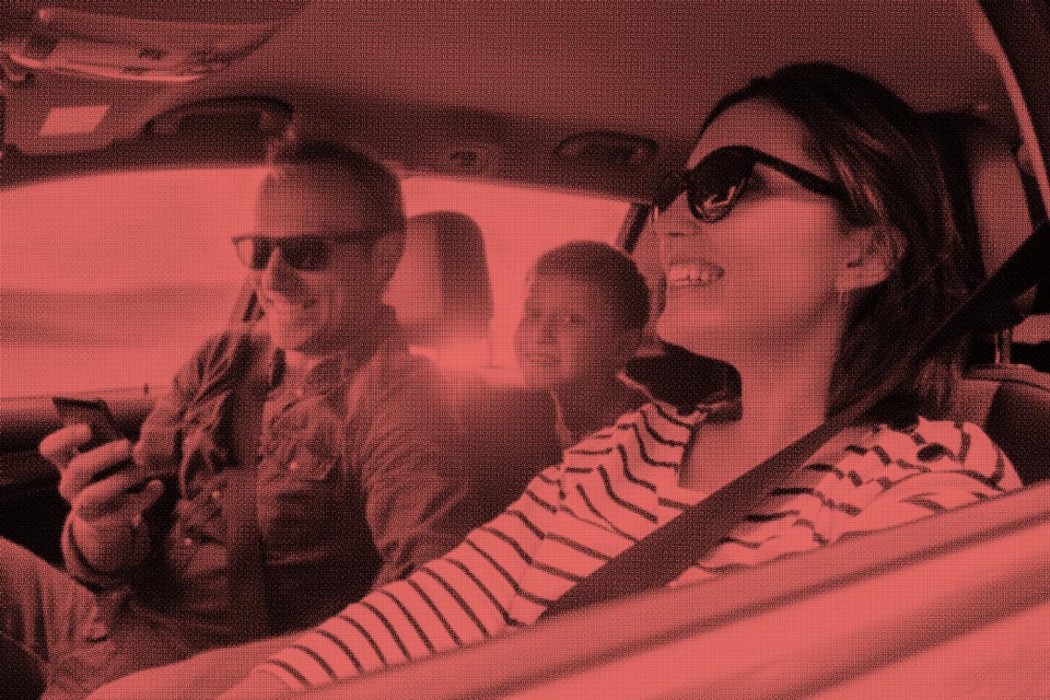 Red & black image of a family smiling and laughing in a car.